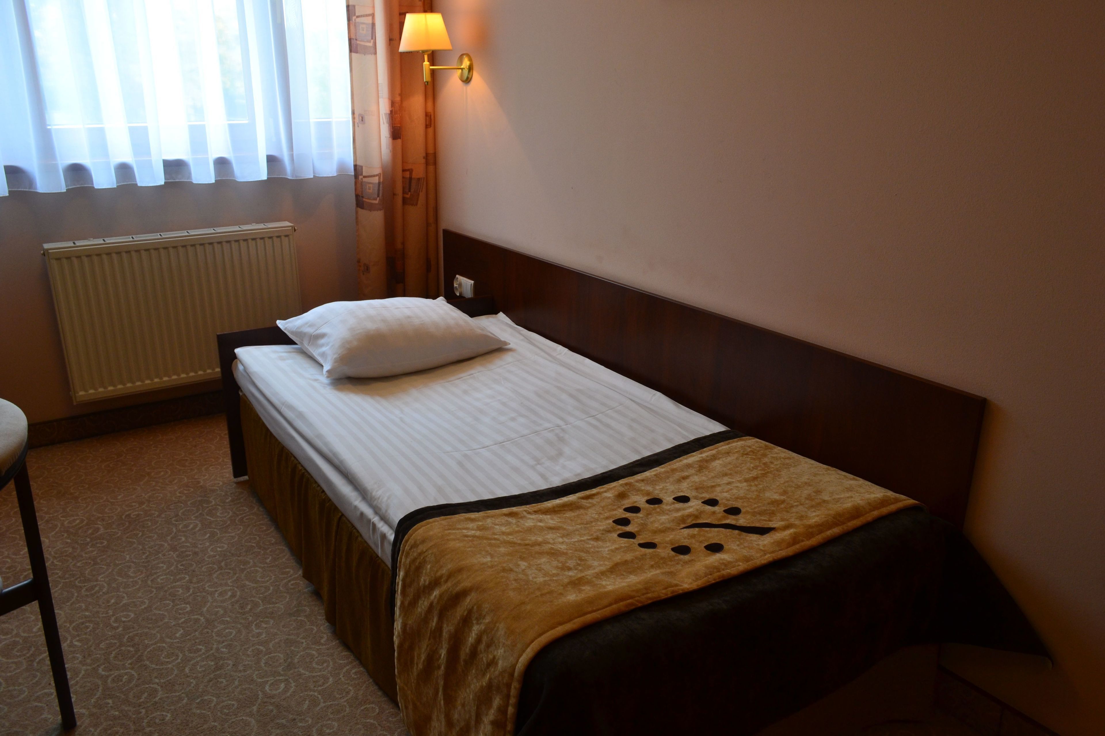 Una habitación de hotel con cama, mesita de noche, lámpara y ventana con cortinas.