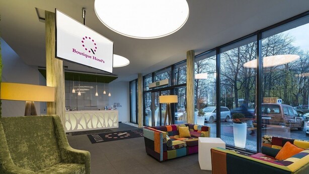 A modern hotel lobby with a reception desk, comfortable seating areas, and large windows offering views of the parking area. - Boutique Hotel's Kwiska / Legnicka (Wroclaw)