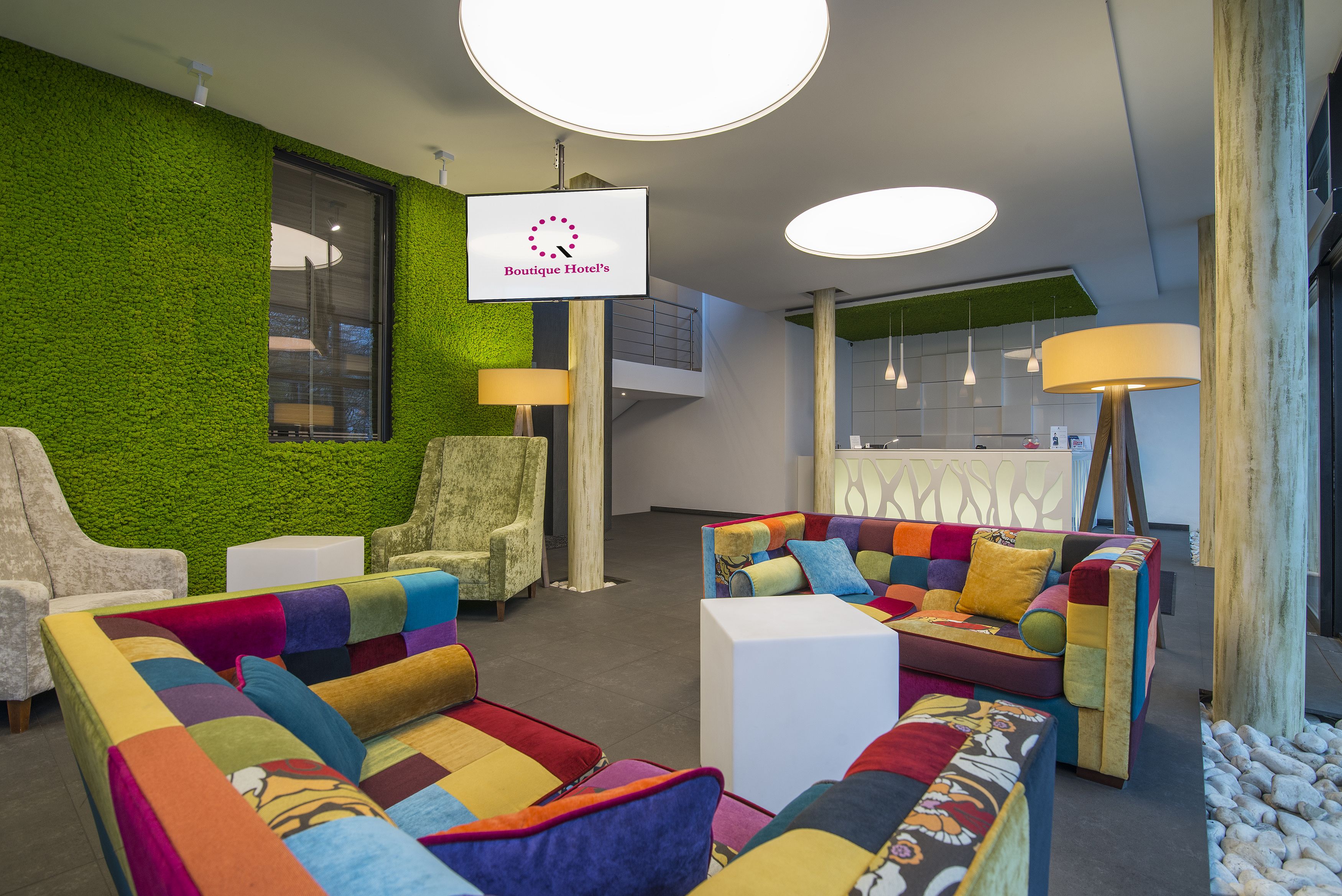 Un hall d’hôtel moderne avec des murs verts, des sièges confortables et une enseigne indiquant « Boutique Hotel ».