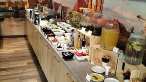 A buffet setup with various food items and beverages, wooden flooring, and a mural of a cityscape in the background. - Boutique Hotel's Kwiska / Legnicka (Wroclaw)