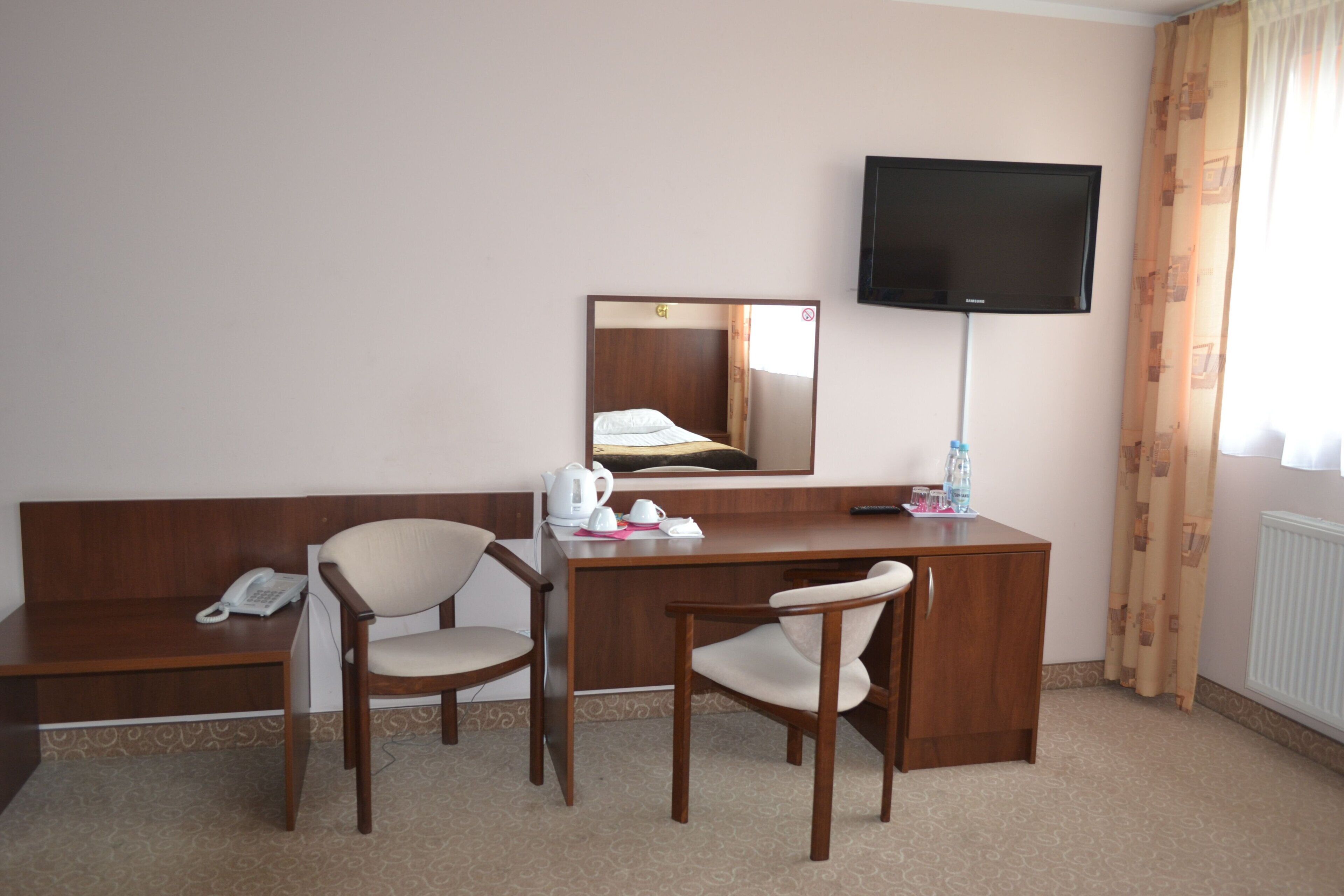 Una habitación de hotel con un escritorio de madera, dos sillas, un teléfono, una televisión y un espejo.