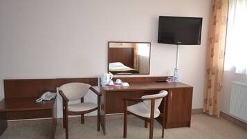 Una habitación de hotel con un escritorio de madera, dos sillas, un teléfono, una televisión y un espejo.