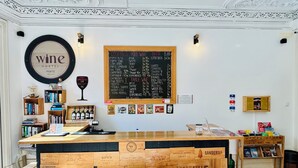 Un bar de vinos acogedor con barra de madera, taburetes y una pizarra con la carta de bebidas y vinos.