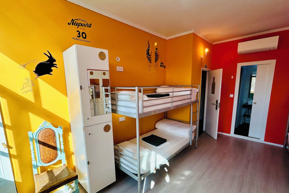 A dormitory room with bunk beds, a wardrobe, a chair, and a wall with a rabbit silhouette and a number '5'.