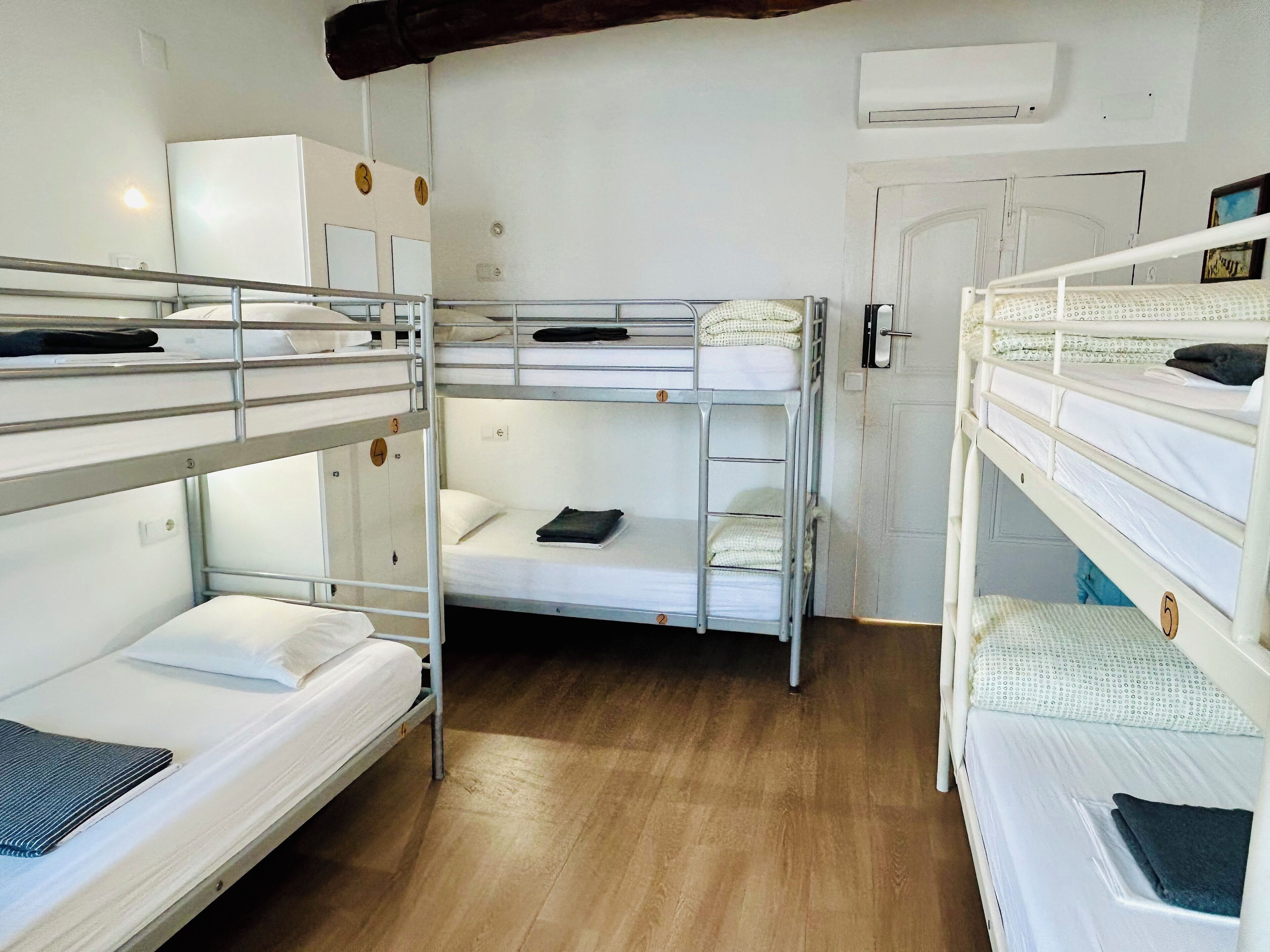 Um quarto de estudante com beliches, um guarda-roupa branco e um ar condicionado.