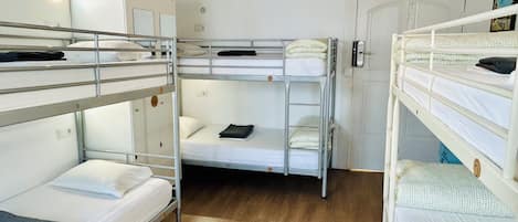 Um quarto de estudante com beliches, um guarda-roupa branco e um ar condicionado.