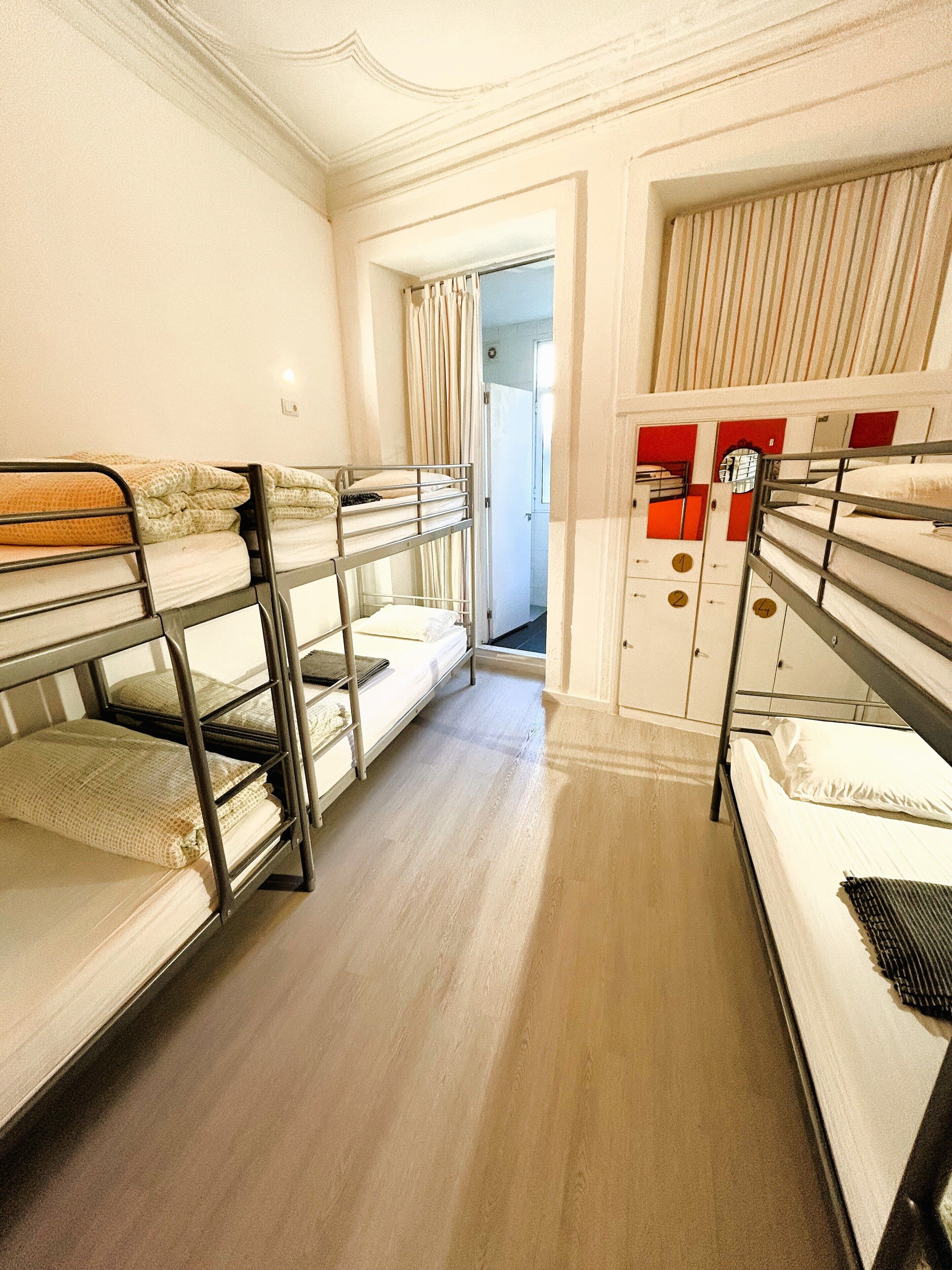 Un dormitorio con literas, suelo de madera y una puerta que da a otra habitación.