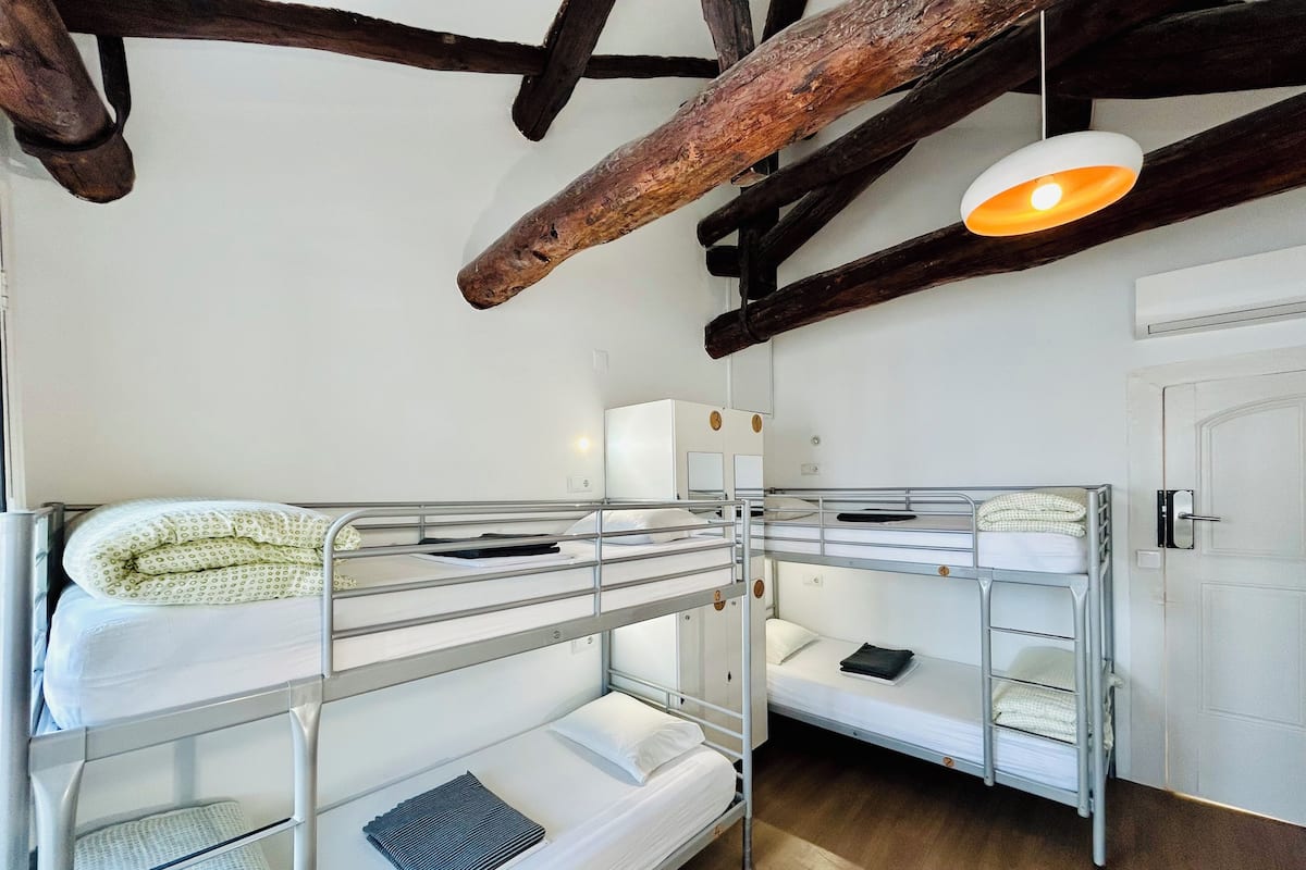 A bunk bed room with a rustic ceiling, a white door, and a bedside lamp.