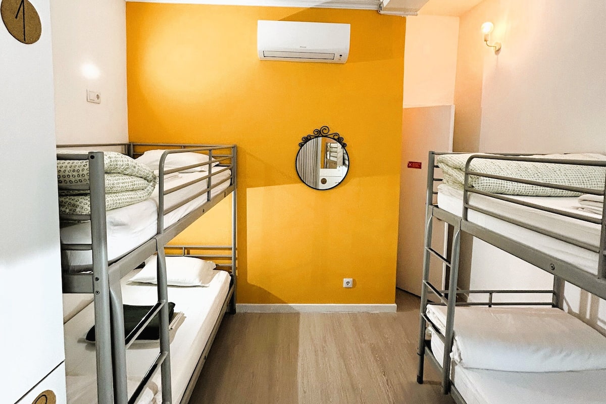 A narrow corridor with bunk beds on either side, a wall-mounted air conditioner, a round mirror, and a light fixture.
