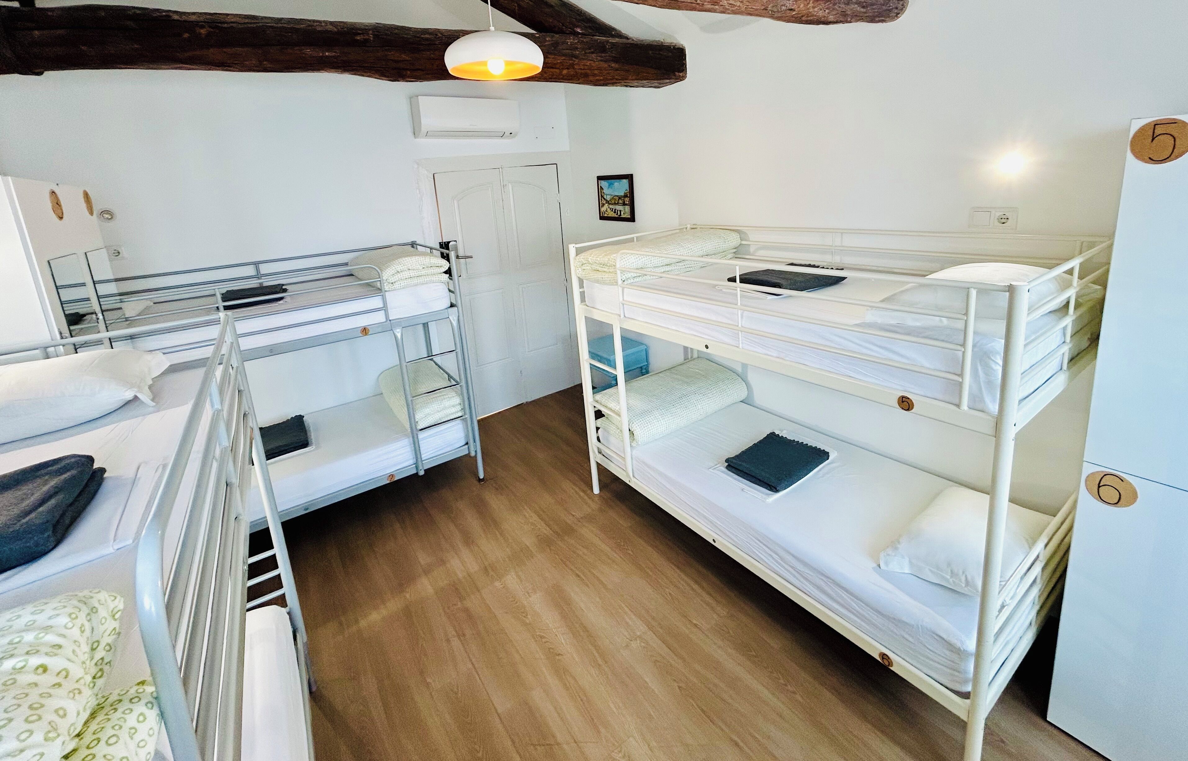 A dormitory room with bunk beds, a wooden floor, a white door, and a small refrigerator.