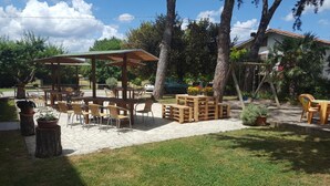 Eine Terrasseneinrichtung im Freien mit Holztischen und -stühlen, umgeben von Bäumen und Blumentöpfen.