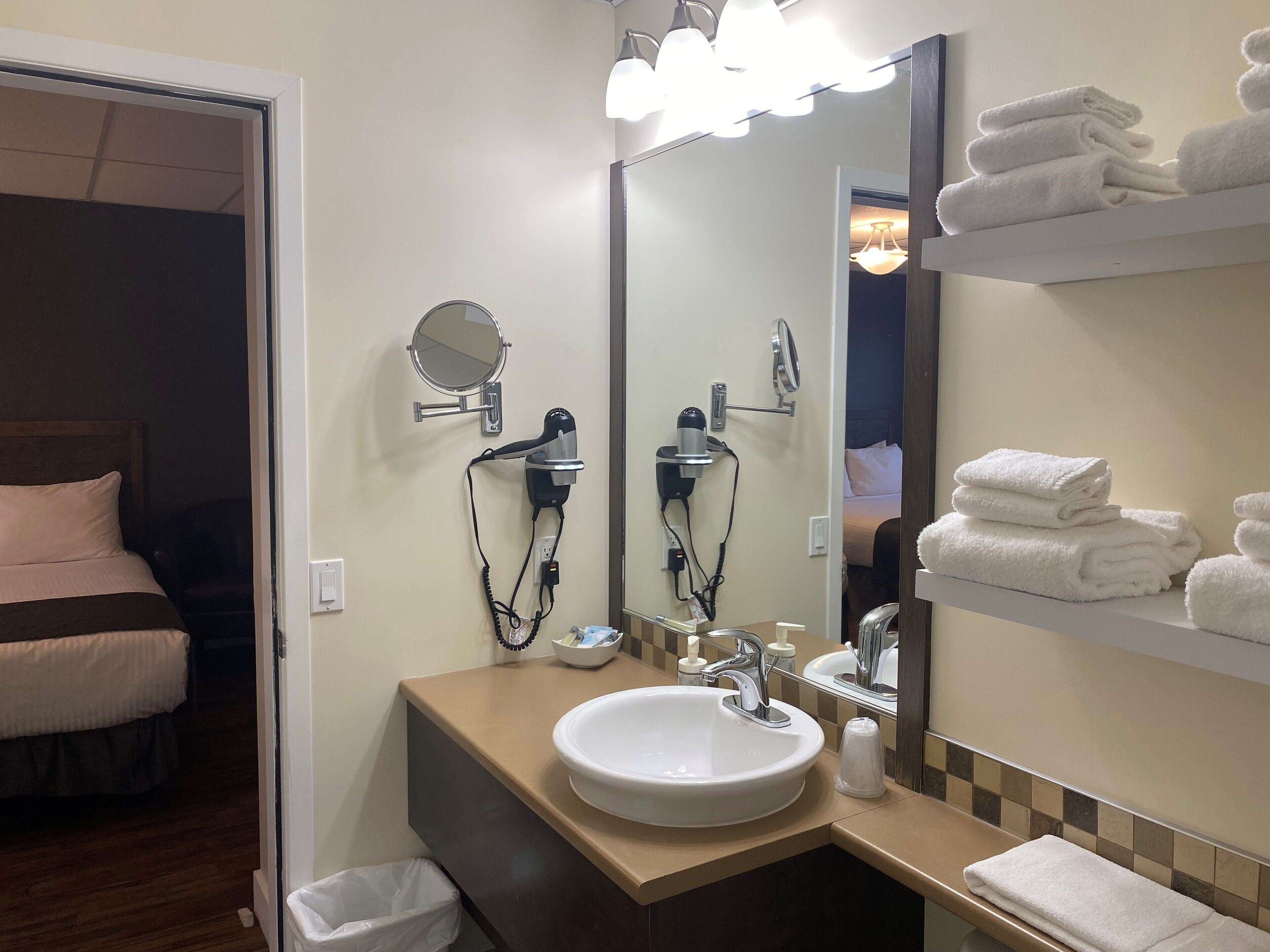Un baño de hotel con lavamanos, espejo, secador de pelo y toallas dobladas en un estante.