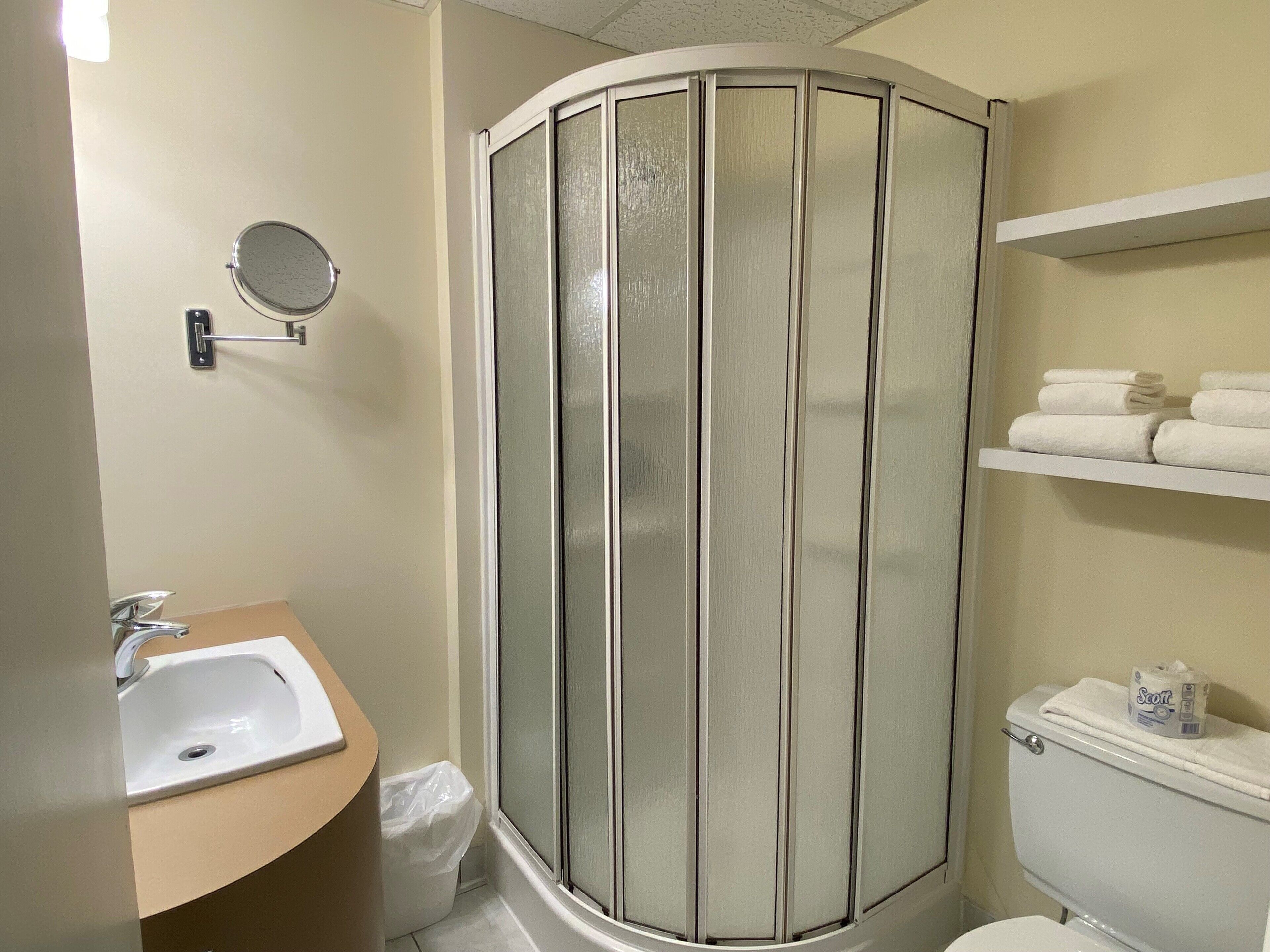 A bathroom with a shower enclosure, a sink, a toilet, and a shelf with towels.