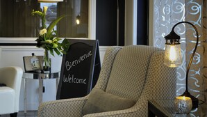 A cozy room with a patterned armchair, a 'Bienvenue' sign, a lamp, and a vase with flowers. - Hôtel Centre-Ville (Montmagny)
