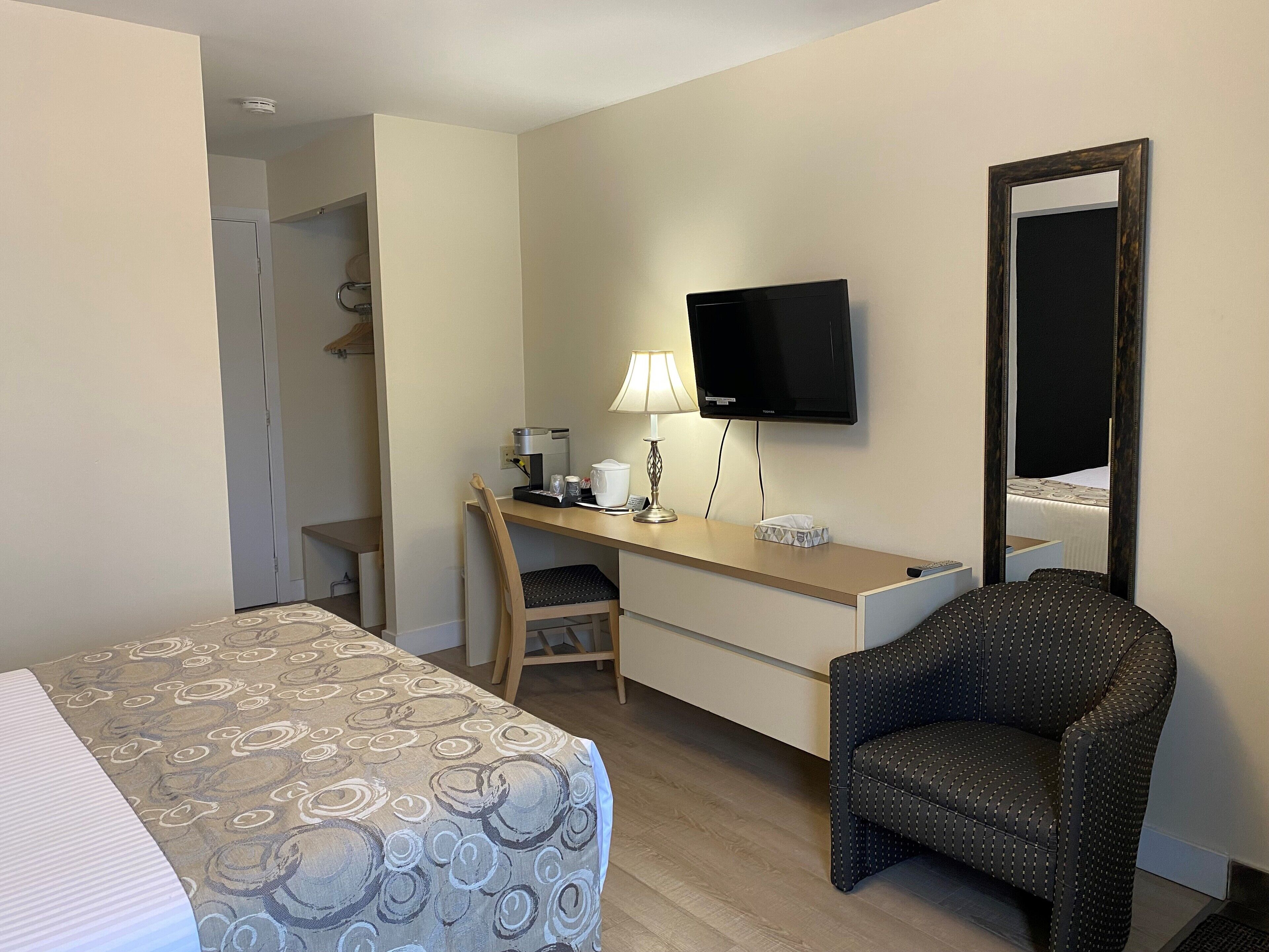 Habitación de hotel con cama, escritorio, silla, televisión y espejo.