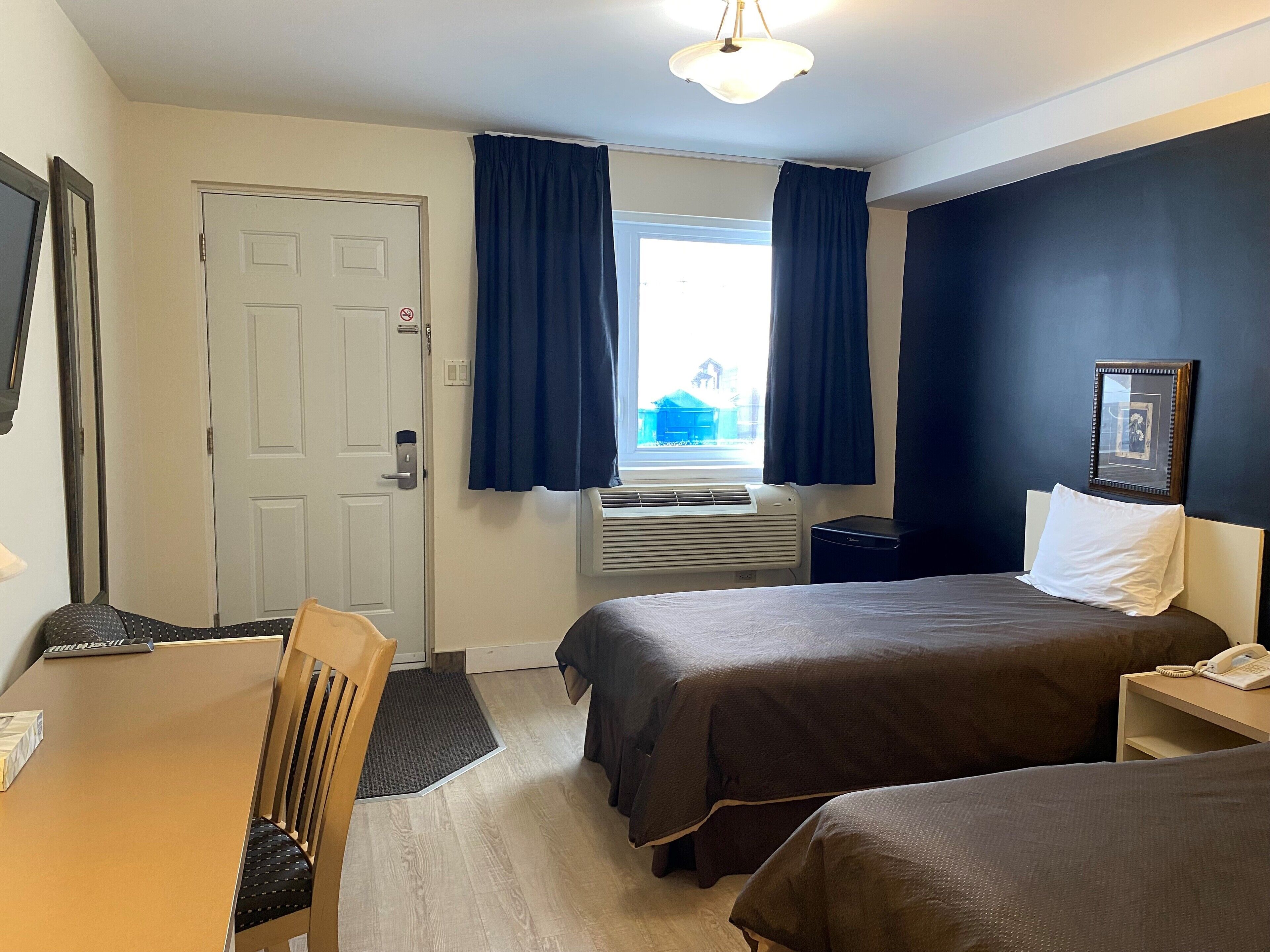 A hotel room with a bed, bedside table, chair, desk, and a window with curtains.