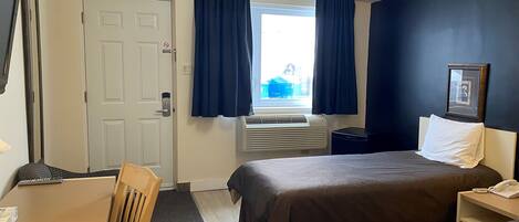 A hotel room with a bed, bedside table, chair, desk, and a window with curtains.