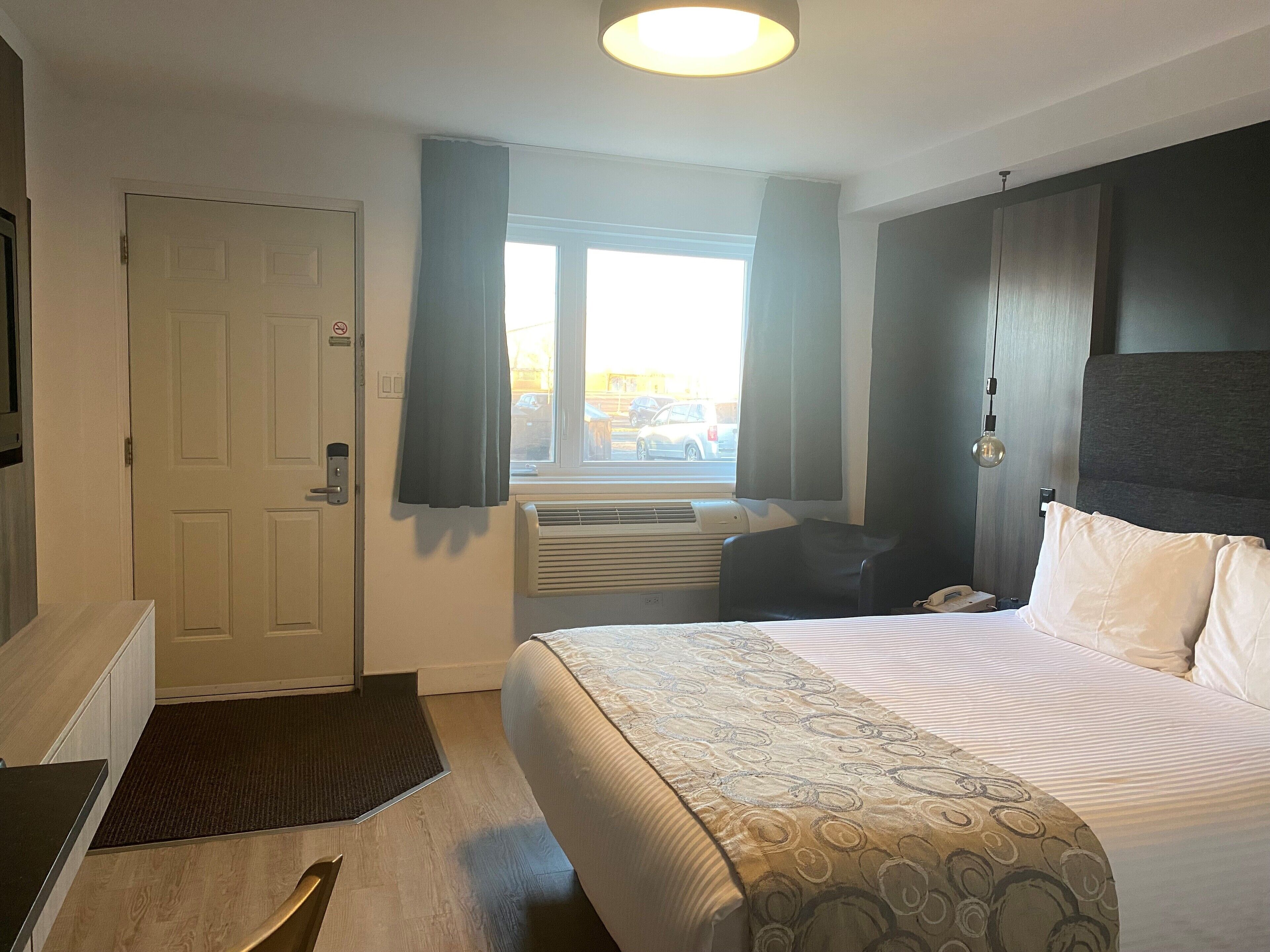 A hotel room with a bed, a desk, a chair, a window with curtains, and a door.