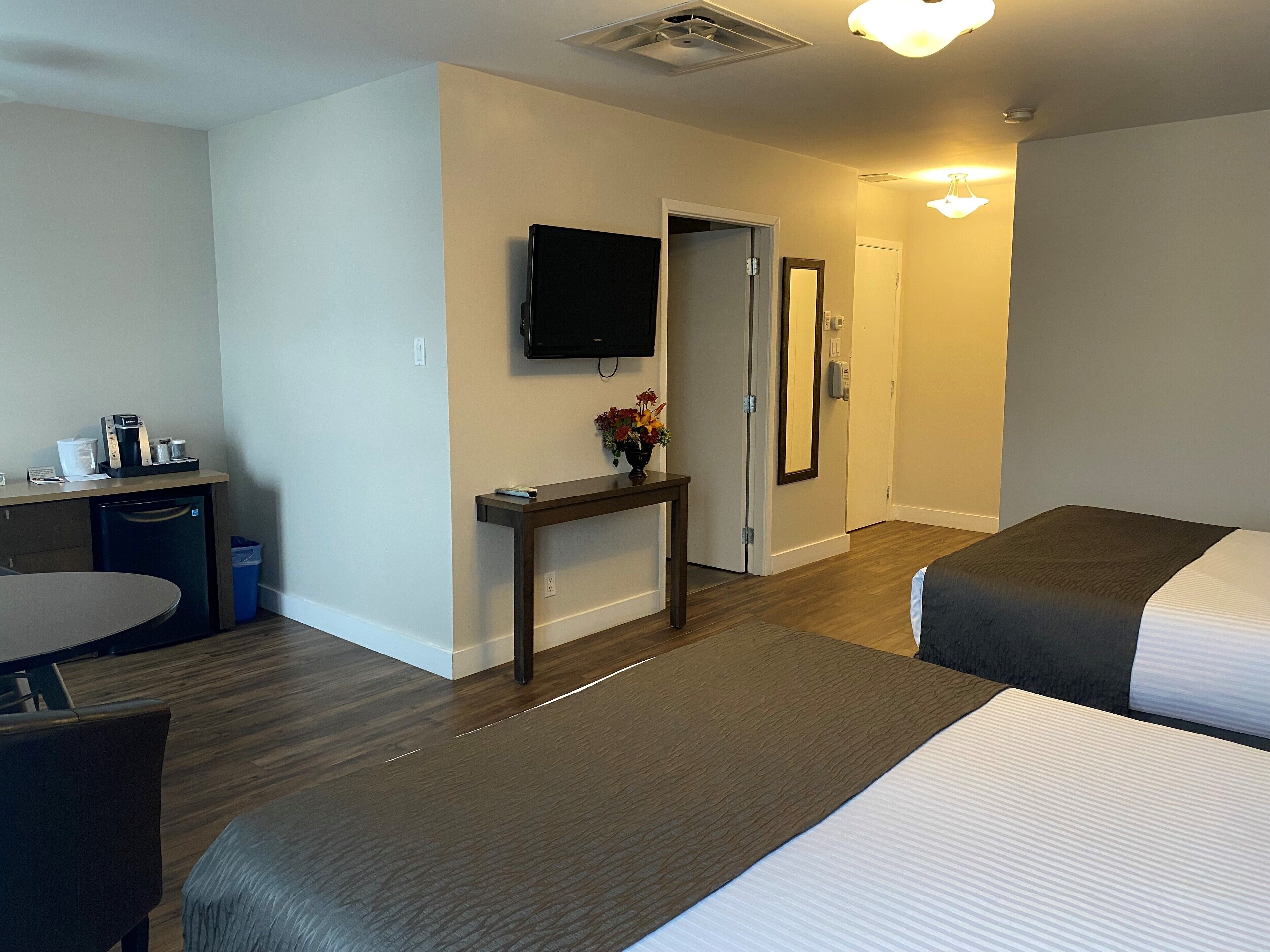 A hotel room with a bed, a desk with a coffee machine, a TV, and a door leading to another room.