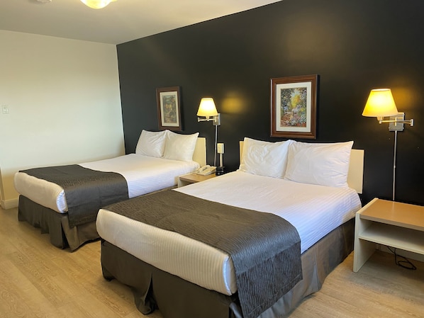 Habitación de hotel con dos camas, cada una con almohada y manta. Se observan mesitas de noche con lámparas y un teléfono instalado en la pared.