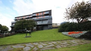 Un edificio moderno con techo plano, varios balcones y un césped bien cuidado con un sendero de piedra.