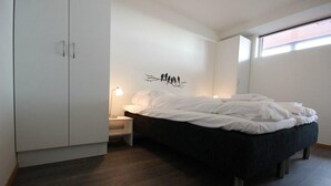 Un dormitorio con cama, armario, mesita de noche, un cuadro de aves sobre una rama y una ventana.
