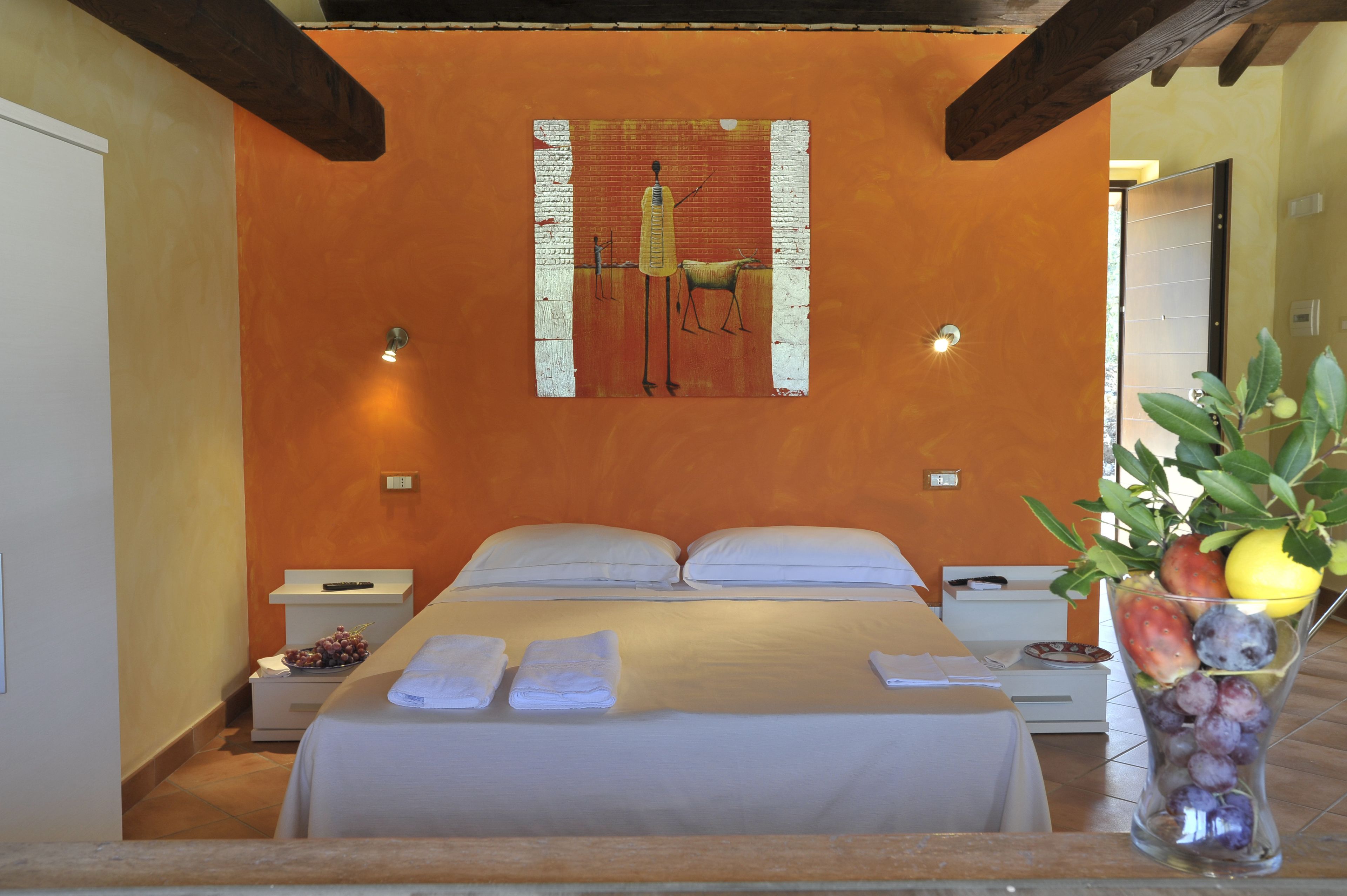 A hotel room with a bed, two bedside tables, a fruit bowl, and a painting on the wall.