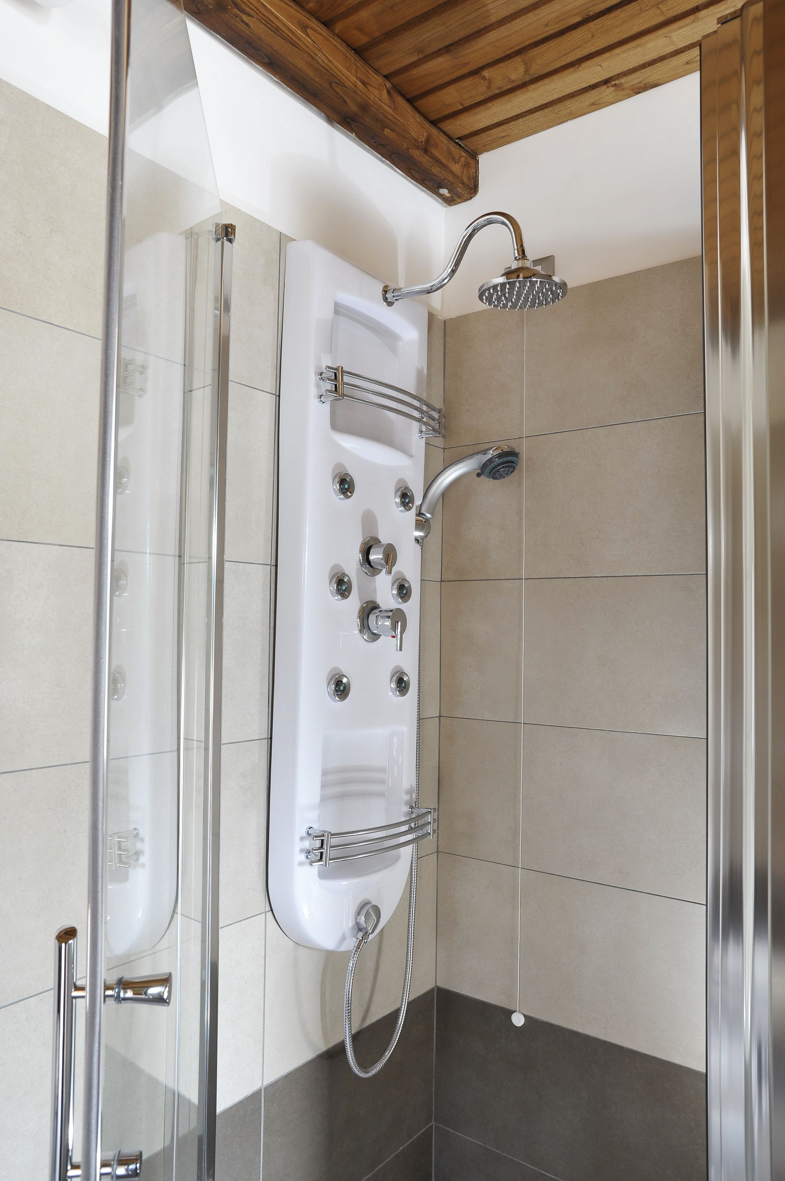 Une douche moderne dotée d’un pare-douche en verre, d’un pommeau de douche à main et de plusieurs boutons de commande.