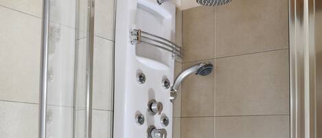 Una ducha moderna con cabina de vidrio, cabezal de ducha de mano y varios mandos.
