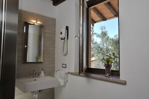 Une salle de bain moderne avec un grand miroir, un lavabo et une fenêtre donnant sur les arbres.