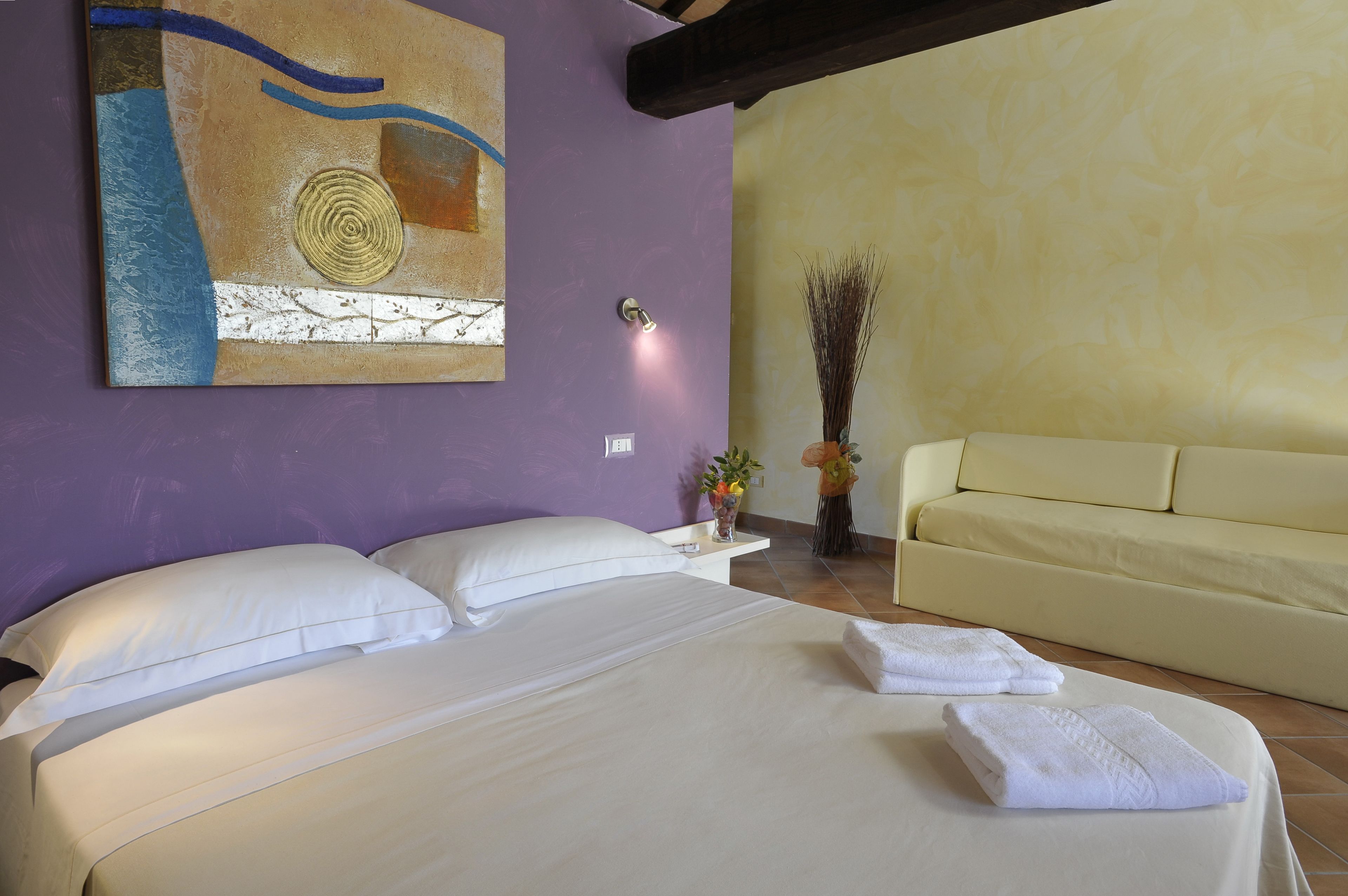 Habitación de hotel con cama, sofá, una obra de arte en la pared, un jarrón con plantas e iluminación empotrada.