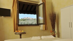 Een hotelkamer met een bed, een klein tafeltje met fruit, een raam met uitzicht op een stad, en een aan de muur bevestigde televisie.
