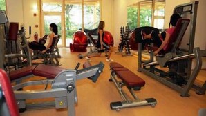 Een sportschool met diverse fitnessapparaten, grote ramen en een houten vloer.
