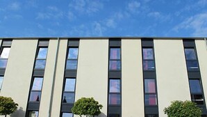 Een modern gebouw met een platte gevel, meerdere ramen en twee kleine bomen ervoor.