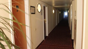Pasillo de hotel con puertas numeradas 229 y 230, un cartel de prohibido fumar y una lámpara circular en la pared.