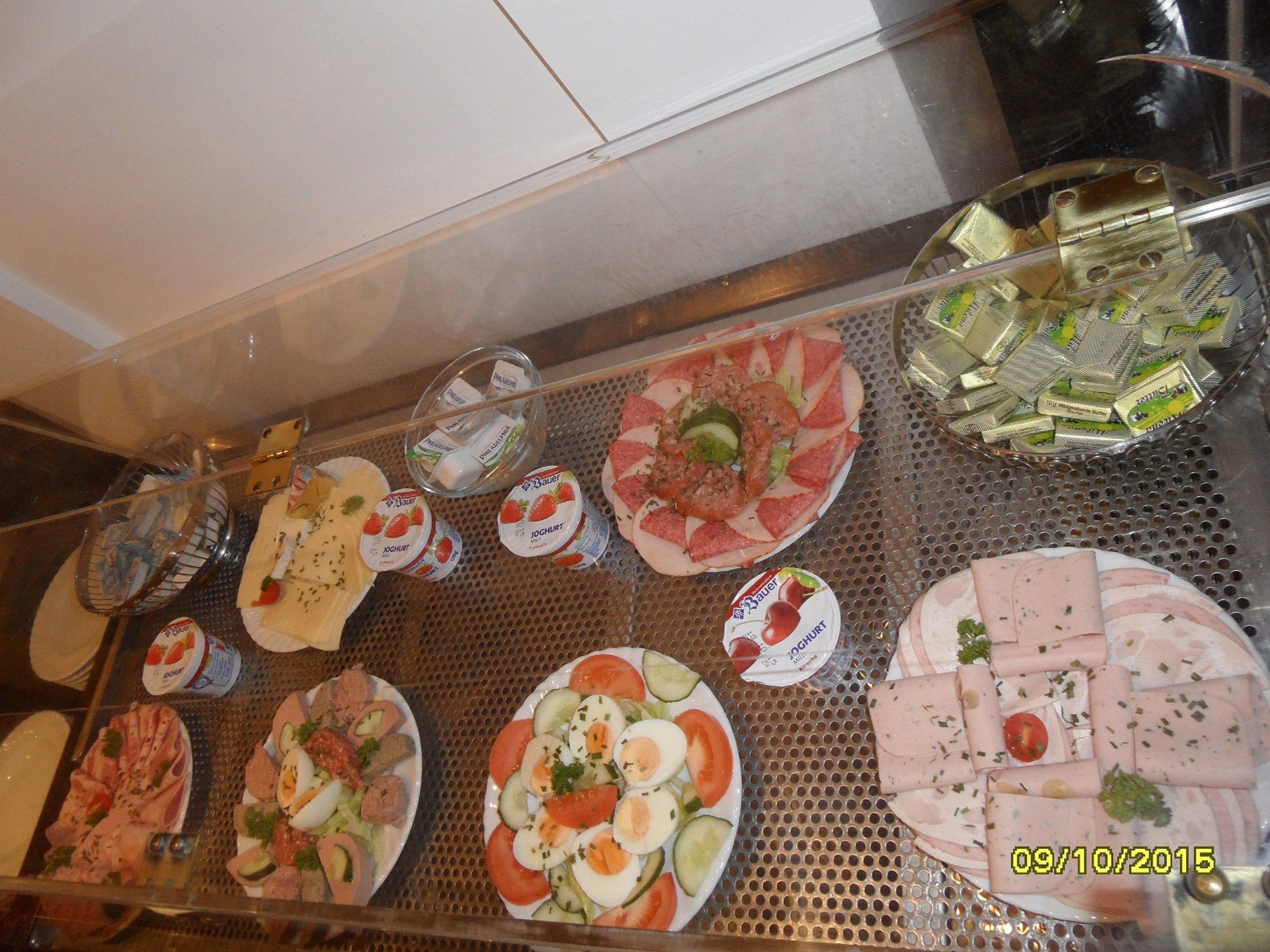 A variety of food items displayed on a metal tray, including plates of sliced meats, cheeses, and vegetables.