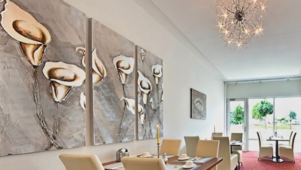 Un comedor moderno con un cuadro abstracto grande, una araña y vistas al exterior.