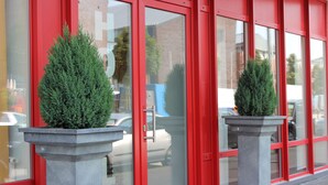 Un edificio con puertas de vidrio de marco rojo y dos plantas de hoja perenne en macetas al frente.