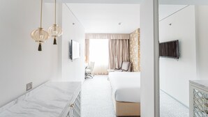 A modern hotel room with a marble bathroom vanity, a large bed with a headboard, a television mounted on the wall, and a large window with curtains. - Dorsett Shepherds Bush (London)