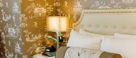 A hotel room with a bed, pillows, a nightstand with a lamp, and a wall with traditional artwork.