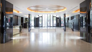 A spacious lobby with a modern ceiling design, a reception desk, and a staircase leading to upper floors. - Dorsett Shepherds Bush (London)