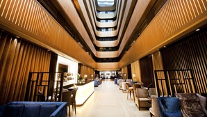 A modern hotel lobby with a central staircase, seating areas, and a reception desk. - Dorsett Shepherds Bush (London)