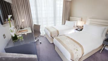 A hotel room with two beds, a desk, a chair, a TV, and a window with curtains.