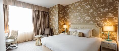 Een hotelkamer met een groot bed, twee nachtkastjes, een stoel, een bureau en een raam met gordijnen.