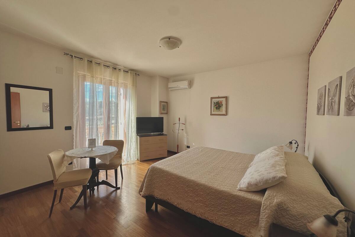 A hotel room with a bed, a desk with a chair, a television, and a window with curtains.