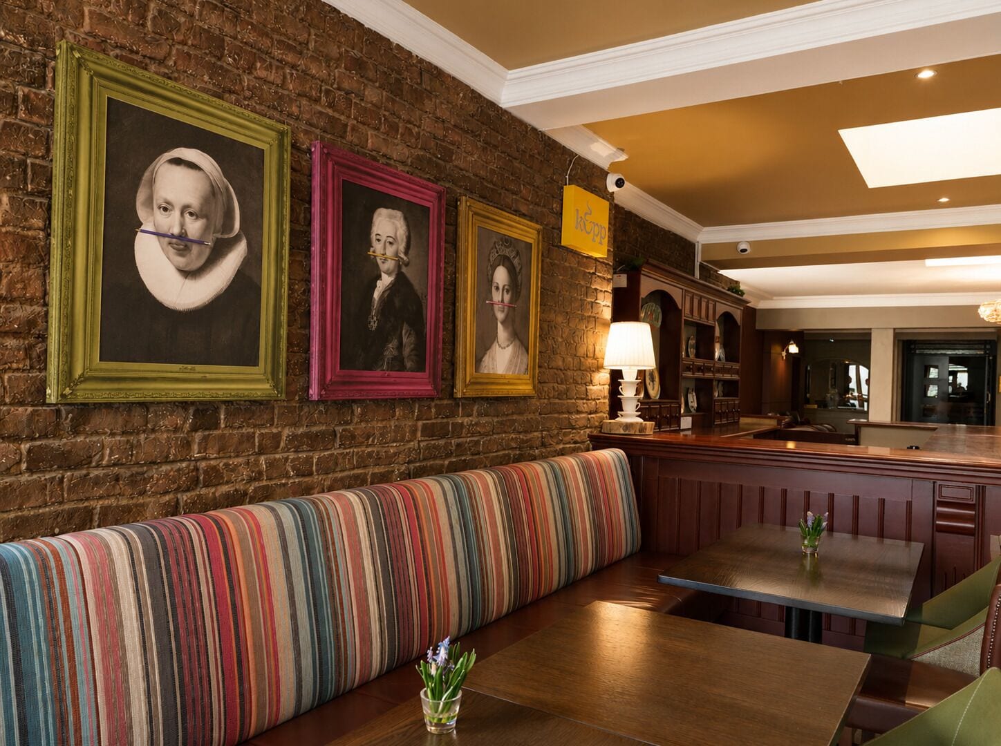 Interior de restaurante con pared de ladrillo, banca a rayas, mesa de madera y retratos enmarcados.