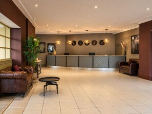 Um saguão de hotel com balcão de recepção, área de estar e elementos decorativos.