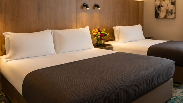 A hotel room with two beds, a wooden headboard, a vase with flowers, and a painting on the wall.