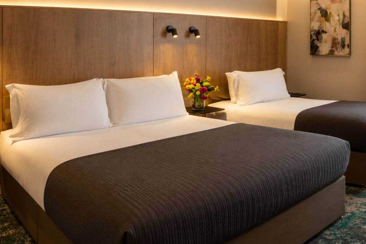 A hotel room with two beds, a wooden headboard, a vase with flowers, and a painting on the wall.