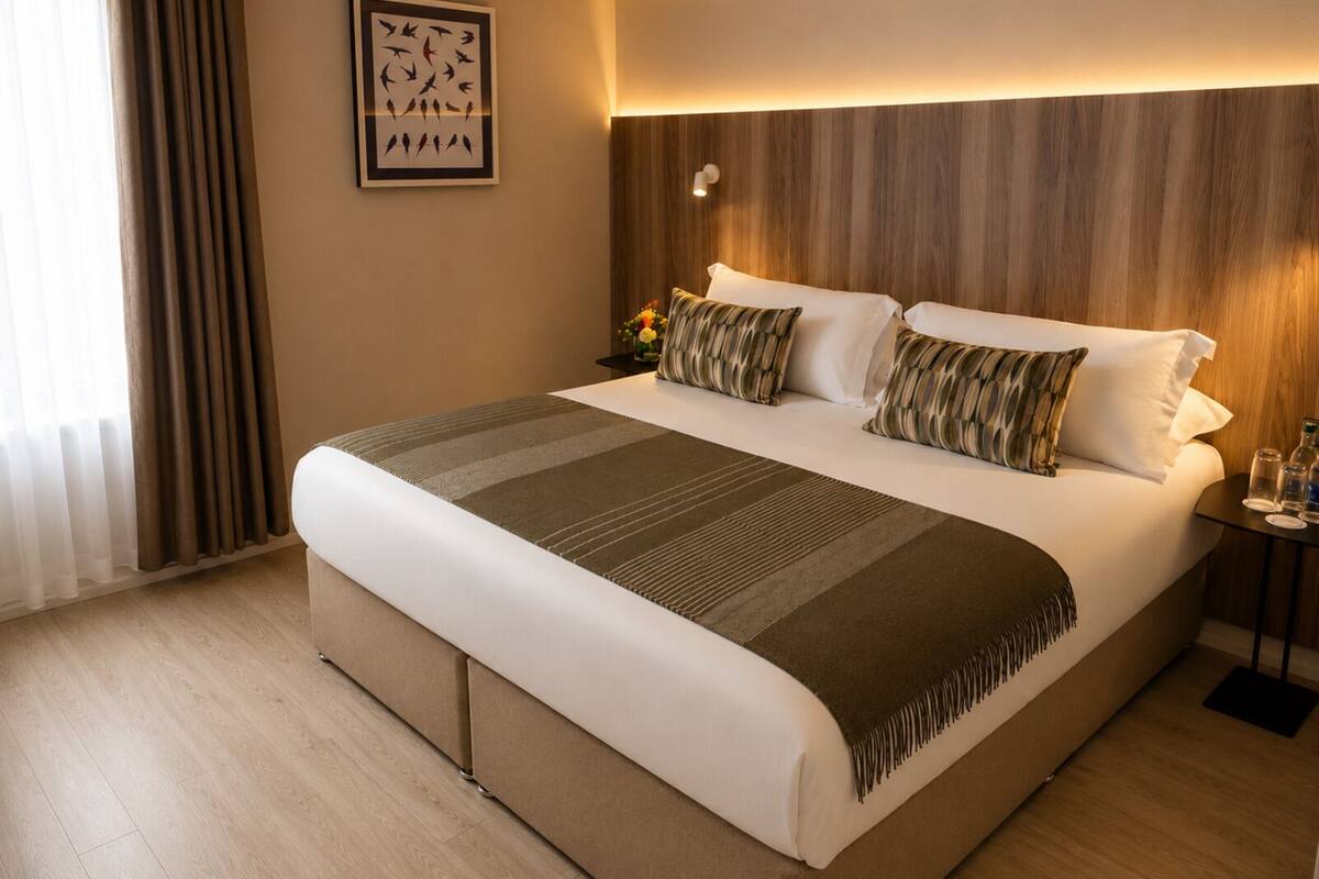 A large bed with a wooden headboard, a bedside table with a lamp, and a framed picture on the wall.